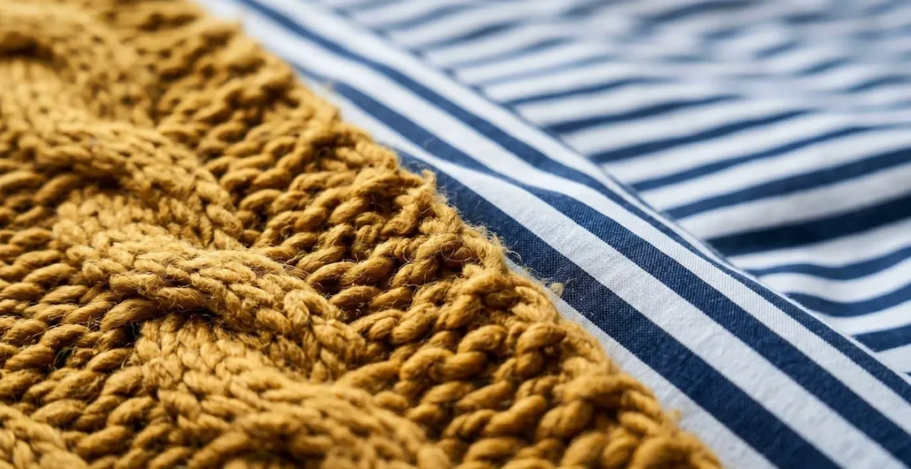 Gros plan sur un plaid uni texturé posé sur une housse de couette rayée créant un point focal apaisant