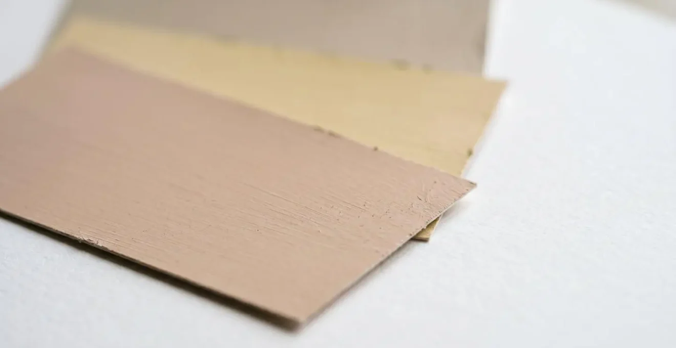 Échantillons de peinture beige avec différents sous-tons comparés à du papier blanc sous lumière naturelle