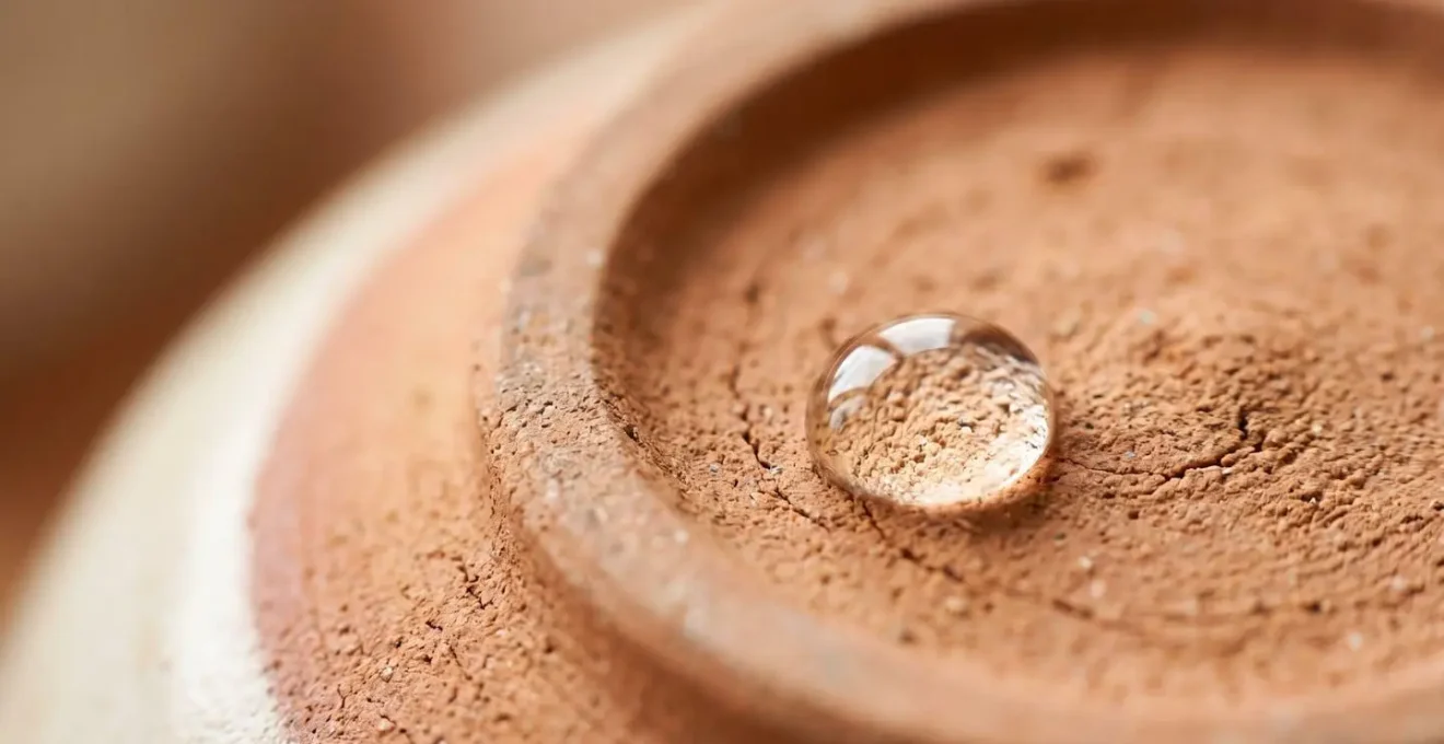 Gros plan macro sur une goutte d'eau déposée sur la base non émaillée d'une céramique artisanale