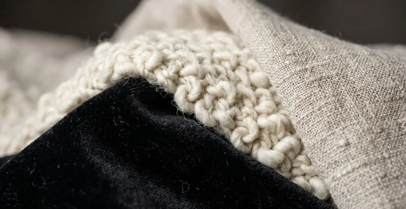 Détail de textures variées en décoration noir et blanc : velours profond, laine bouclée et lin naturel créant de la profondeur
