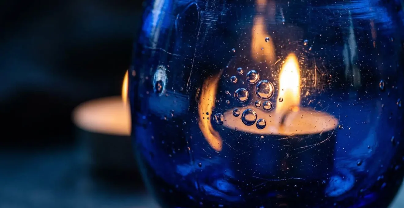 Gros plan sur un verre artisanal bleu cobalt contenant une bougie, révélant les bulles et la diffraction de la lumière